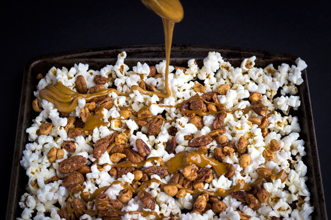 Drizzling caramel sauce over popcorn mixture on sheet pan
