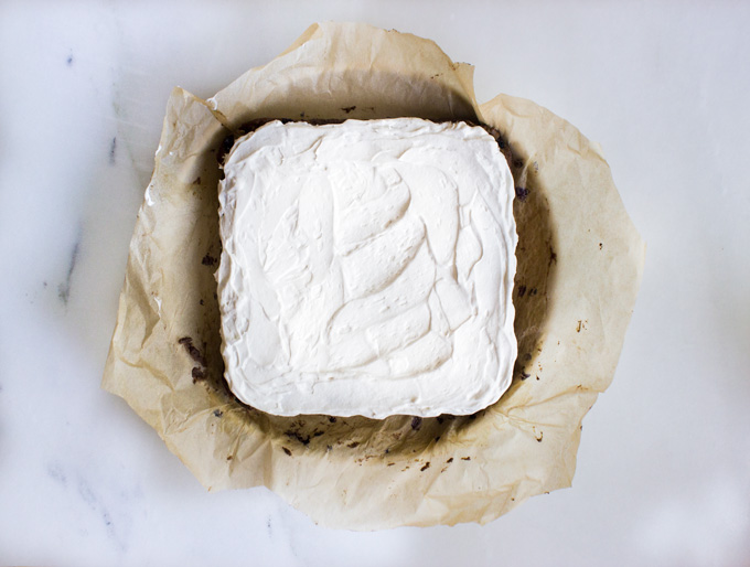 Overhead view of a square cake with white frosting placed in a round baking pan with parchment paper